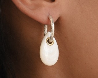 May include: Silver hoop earrings with a white teardrop-shaped pendant. The pendant has a gold accent.