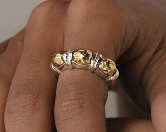 May include: A silver ring with three gold, textured, round accents.