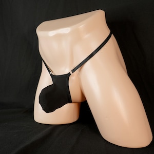 May include: Black thong underwear with a pouch, displayed on a mannequin. The thong features thin straps and a pouch that covers the front. The background is black.