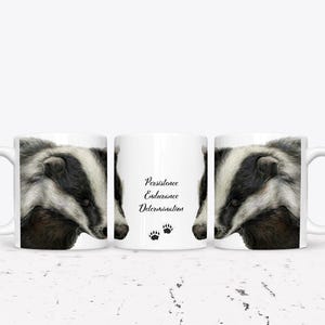 Può includere: Tre tazze in ceramica bianca con un'illustrazione di tasso su ogni lato. La tazza al centro ha le parole "Persistenza, Resistenza, Determinazione" e due impronte di zampe.