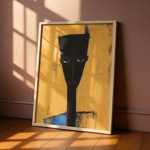 May include: A framed wall art print featuring a stylised, elongated black figure with a flat-topped head and neutral expression set against a textured mustard yellow background, with a small blue rectangular shape at the base of the figure's neck.