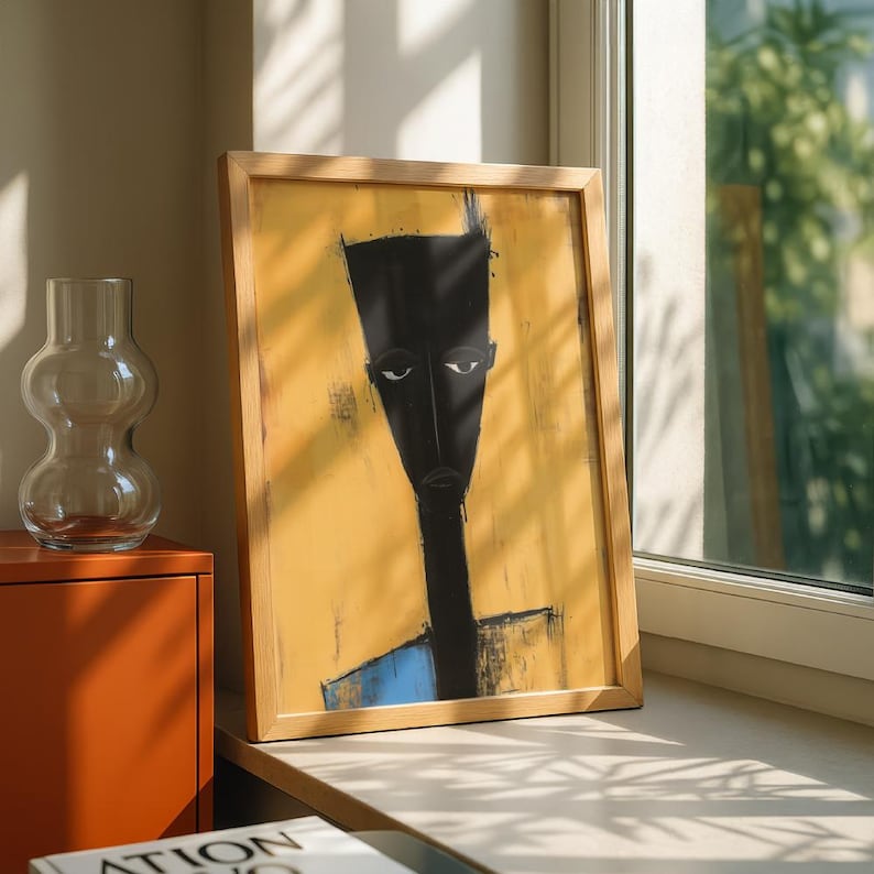 May include: A framed rectangular wall art piece featuring a stylised, elongated black figure with a flat-topped head against a textured mustard yellow background. The figure has a long neck and a small blue section at the bottom, all encased in a light wood frame.