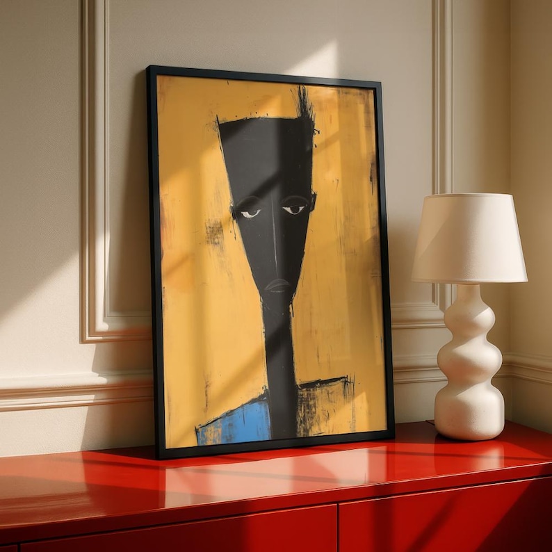 May include: A framed vertical wall art print featuring a stylised, elongated black figure with a flat-topped head against a textured mustard yellow background, with a small blue accent at the bottom, enclosed in a thin black rectangular frame.