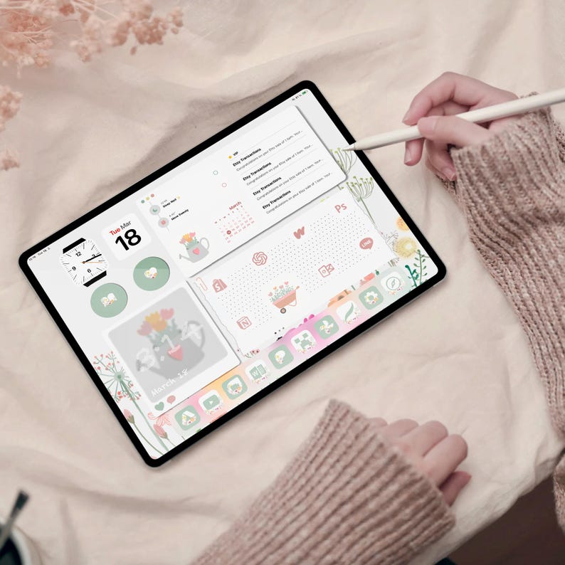 May include: A digital tablet with a floral design and a calendar app open. The tablet is on a light pink surface and a hand is holding a stylus pen.