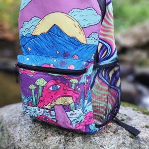 Może przedstawiać: Kolorowy plecak z psychodelicznym wzorem przedstawiającym grzyba, góry i słońce. Plecak ma siatkową kieszeń z boku i kieszeń zapinaną na zamek błyskawiczny z przodu.
