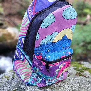 May include: A psychedelic backpack with a purple, pink, blue, and green design. The backpack features a mountain scene with a sun and clouds, as well as mushrooms and a three-eyed creature.
