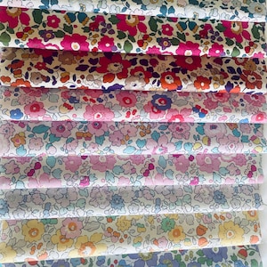 Puede incluir: Una pila de diez muestras de tela dobladas, cada una con un patrón floral distinto con varias paletas de colores que incluyen verde azulado, magenta, naranja, rosa, lavanda, amarillo, azul y verde, dispuestas verticalmente.