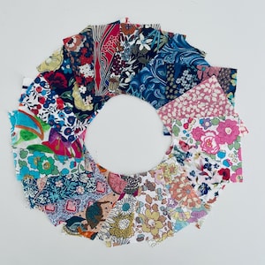 May include: A collection of 15 fabric squares with various floral patterns in shades of pink, blue, green, red, and white. The squares are arranged in a circle.