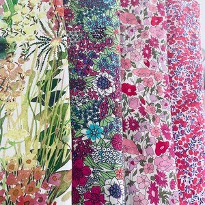 Pode incluir: Exibição vertical de quatro rolos de tecido com estampas florais. O primeiro rolo apresenta um design em estilo aquarela com flores amarelas, rosas e verdes. Os outros rolos exibem estampas florais vibrantes em tons de rosa, vermelho e azul.