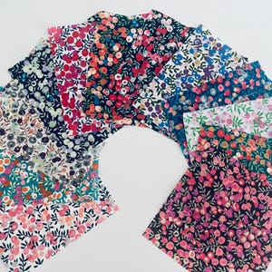 May include: A collection of square fabric swatches arranged in a fan shape, each featuring distinct floral patterns with various colour palettes including pink, red, blue, green, and white, showcasing dense botanical prints with small blossoms and leaves.