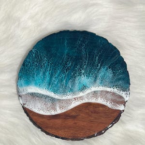 May include: A round wooden coaster with a teal blue and white resin ocean wave design.