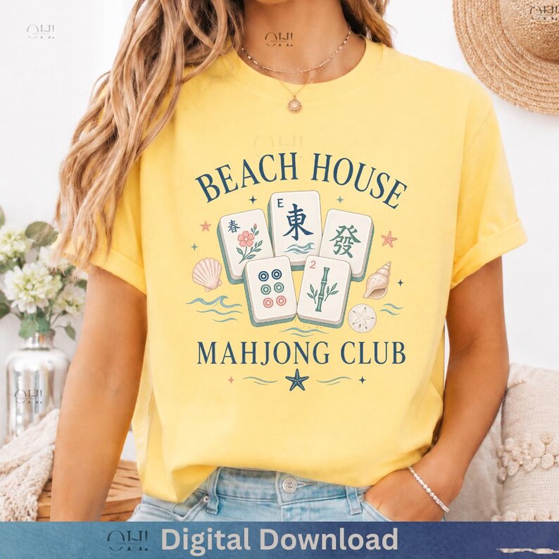 May include: Yellow t-shirt with a graphic design featuring the words "BEACH HOUSE MAHONG CLUB" and illustrations of Mahjong tiles, seashells, and stars. The shirt has short sleeves and a crew neck.