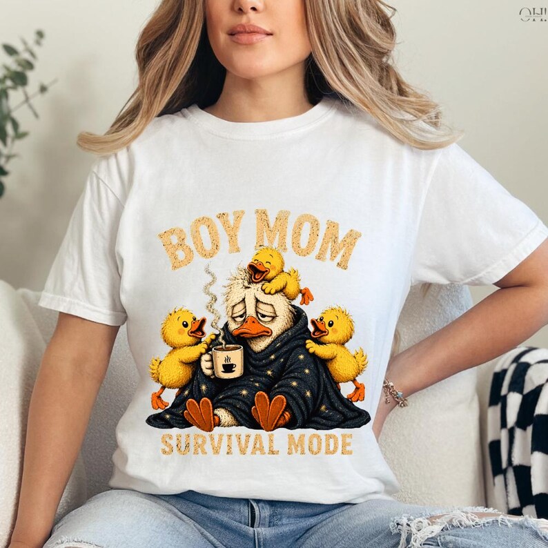 May include: White t-shirt with a humorous graphic featuring a tired duck wrapped in a blanket, holding a coffee cup, surrounded by yellow ducklings. The text "BOY MOM" and "SURVIVAL MODE" are printed above and below the duck illustration.