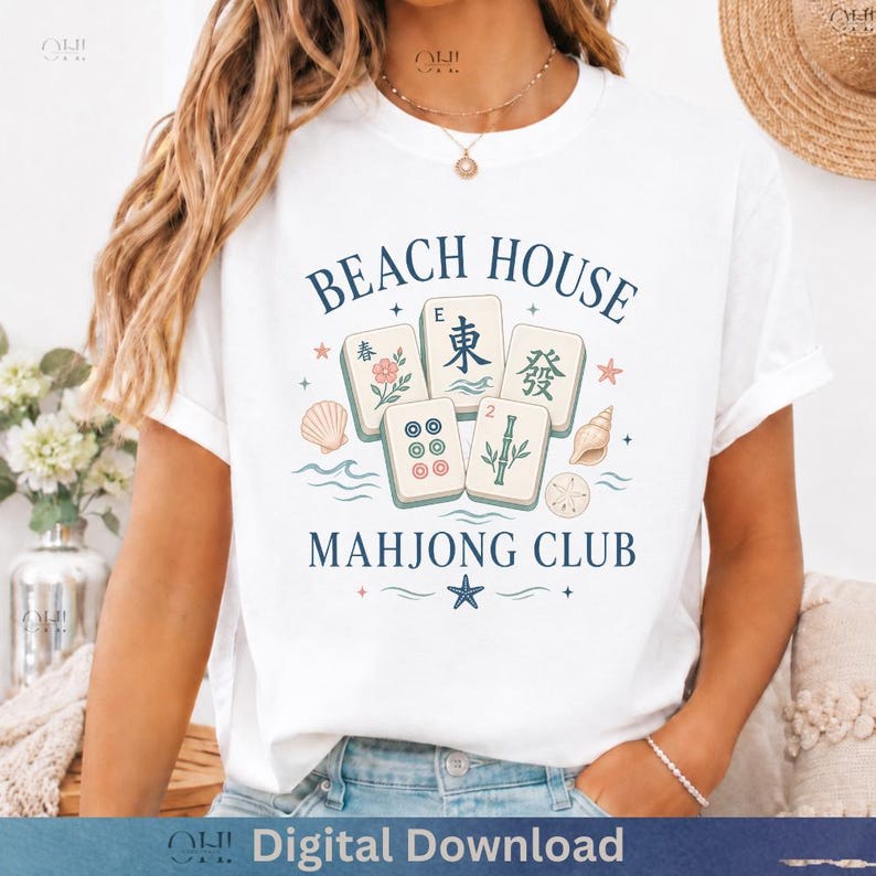 May include: White t-shirt with a "Beach House Mahjong Club" design. The graphic features mahjong tiles, seashells, and the text "Beach House Mahjong Club" in navy blue. The shirt has short sleeves.