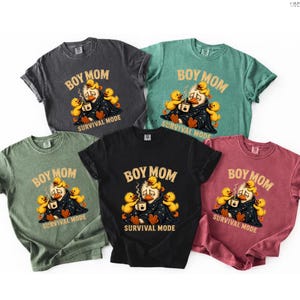 May include: A collection of five t-shirts in various colors, including black, green, and maroon. Each shirt features a graphic of a duck surrounded by ducklings, with the text "BOY MOM" and "SURVIVAL MODE".