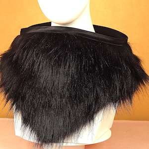 May include: A black faux fur collar with a satin band at the neckline. The collar is displayed on a white mannequin head against a warm-toned background. The fur is long and textured, creating a dramatic look.