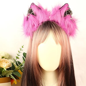Op de afbeelding: Een hoofdband met pluizige roze nepbont kattenoren. De oren zijn gedetailleerd met zwart leer, zilveren sterbedels en kettingen. De hoofdband wordt getoond op een mannequinhoofd met roze en bruin haar.