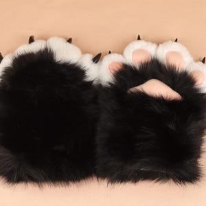 Puede incluir: Un par de calentadores de manos de piel sintética negra y blanca con garras negras.