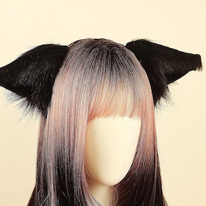 May include: Black faux fur cat ears headband. The ears are triangular and fluffy, attached to a black headband. The mannequin head has long hair with a gradient of black, pink, and blonde.
