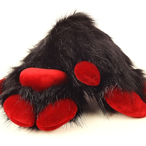 May include: A plush black furry paw with five red pads. The faux fur is long and shaggy, and the pads are a smooth, velvety material. The paw is designed to look like an animal's paw.