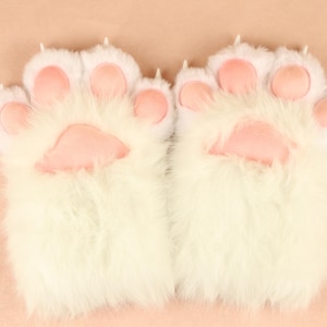 Puede incluir: Un par de calentadores de manos de pata de gato blancos y peludos con almohadillas rosas.