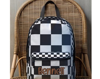 May include: Black and white checkered backpack with the name "Bennett" in brown lettering. The backpack has a front pocket with a zipper and a black handle. The bag is sitting on a wicker chair.