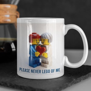 May include: White ceramic mug with a graphic of two Lego figures holding a red heart. The text "PLEASE NEVER LEGO OF ME" is printed on the mug.