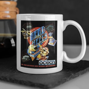 Può includere: Tazza in ceramica bianca con un'immagine in bianco e nero del videogioco Head Over Heels. L'immagine presenta due cani dei cartoni animati e il testo "Head Over Heels" e "Ocean".