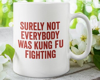 Puede incluir: Taza de cerámica blanca con una inscripción roja que dice "Seguramente no todo el mundo estaba luchando kung fu". La taza está sobre una superficie texturizada blanca y marrón con flores blancas.