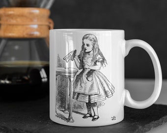 May include: White ceramic mug featuring a black and white illustration of Alice from Alice in Wonderland. The illustration shows Alice holding a bottle with the word "DRINK" on it. A coffee maker is in the background.