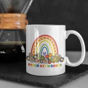May include: White ceramic mug with a rainbow and flowers design. The text "Proud Keyworker" is printed on the mug.