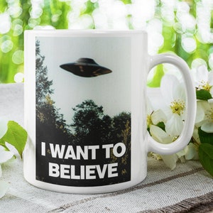 Może przedstawiać: Biały ceramiczny kubek do kawy z czarno-białym obrazkiem UFO i tekstem "I WANT TO BELIEVE".