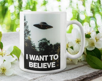 May include: White ceramic coffee mug with a black and white image of a UFO and the text "I WANT TO BELIEVE".