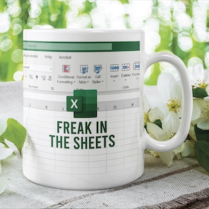 Könnte beinhalten: Ein weißer Keramikbecher mit einem aufgedruckten Grafikdesign einer Microsoft Excel-Tabellenoberfläche. Das Design enthält das grüne Excel-Logo und den Text "FREAK IN THE SHEETS" in dunkelgrünen Großbuchstaben mittig auf dem Becher.