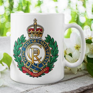Peut inclure: Mug en céramique blanche avec l'emblème des Royal Engineers. L'emblème comprend une couronne, une couronne de laurier et du texte. La tasse a une anse incurvée. Fond flou avec des fleurs blanches.