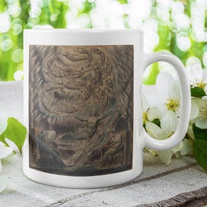 Könnte beinhalten: Weiße Keramiktasse mit einer detaillierten Sepia-Illustration. Das Kunstwerk zeigt eine klassische Szene mit Figuren und wirbelnden Elementen. Die Tasse steht vor einem verschwommenen grünen Hintergrund mit weißen Blumen.