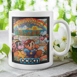 May include: White ceramic coffee mug with a colorful illustration of a video game character and the text "Rainbow Island" and "Ocean".