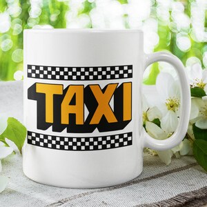 Może przedstawiać: Biały kubek ceramiczny z czarno-białą kratką i napisem "TAXI" żółtymi literami.