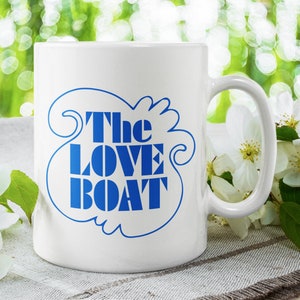 Könnte beinhalten: Weiße Keramiktasse mit einer blauen Grafik der Worte "The Love Boat" in einer stilisierten Schrift.