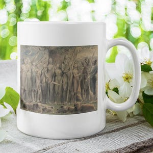 May include: White ceramic mug with a sepia-toned image of a classical relief sculpture. The image shows figures in flowing garments. The mug has a curved handle and a smooth, glossy finish. The background is blurred with green and white bokeh.