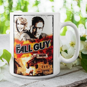 May include: White ceramic mug with a colorful image of a movie poster for "The Fall Guy" featuring a man and woman in front of a car explosion.