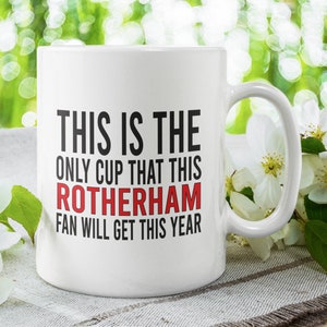 Peut inclure: Une tasse en céramique blanche avec du texte noir qui dit "This is the only cup that this Rotherham fan will get this year". Le texte "Rotherham" est en rouge.