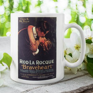 May include: White ceramic mug with a black and white image of a movie poster for the film "Braveheart" starring Rod La Rocque. The poster features a couple embracing and kissing. The text on the poster reads "Cecil B. De Mille Presents Rod La Rocque in "Braveheart" Lillian Rich, Robert Edeson, Tyrone Power, Jean Acker. From the play "Strongheart" by William C. De Mille. Alan Hale Producers. Distributing Corporation."
