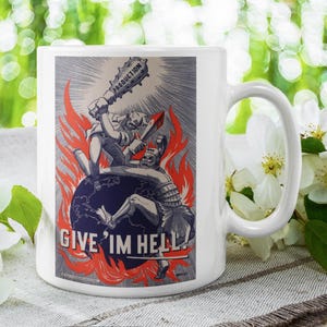 May include: White ceramic mug featuring a vintage illustration of two figures battling on a globe, with flames and the text "GIVE 'IM HELL!". The mug has a large handle and a glossy finish, perfect for coffee or tea.