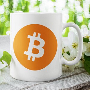Könnte beinhalten: Eine weiße Keramiktasse mit einem orangenen Kreis und einem weißen Bitcoin-Symbol. Die Tasse steht auf einer weißen und braunen strukturierten Oberfläche mit weißen Blumen.