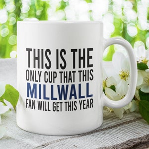 Peut inclure: Une tasse en céramique blanche avec un motif noir et bleu. Le texte sur la tasse est "This is the only cup that this Millwall fan will get this year."