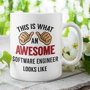 May include: White ceramic mug with a black and red design that says "This is what an awesome software engineer looks like". The mug has two thumbs up pointing towards the word "awesome".