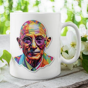 May include: White ceramic mug with a colorful portrait of a man wearing glasses. The mug is sitting on a white and gray surface with white flowers.