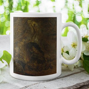 May include: White ceramic coffee mug featuring a brown and tan abstract design. The mug is set against a blurred green background with white flowers and green leaves.