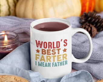 May include: White ceramic mug with a brown liquid inside. The mug has a retro-style design with the text "WORLD'S BEST FARTER I MEAN FATHER" in yellow, red, and blue.